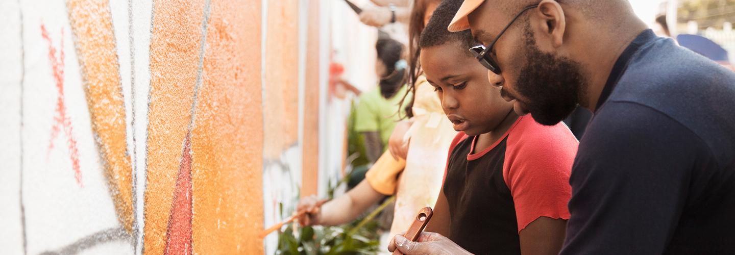 a father and son help paint a mural