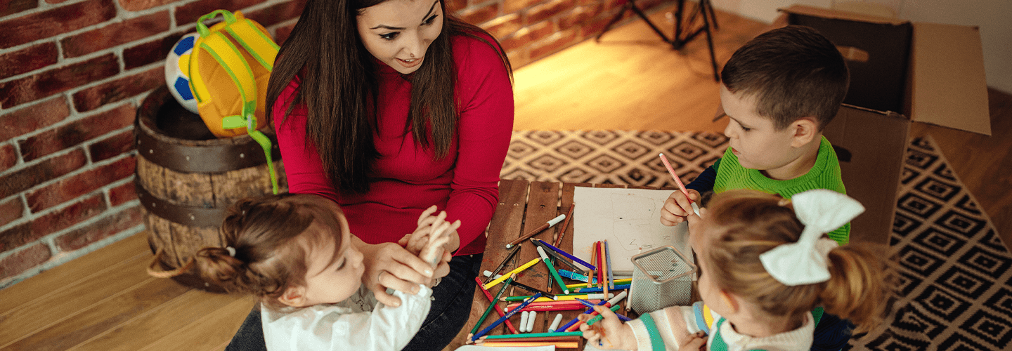 Woman sits at table with children in child care setting