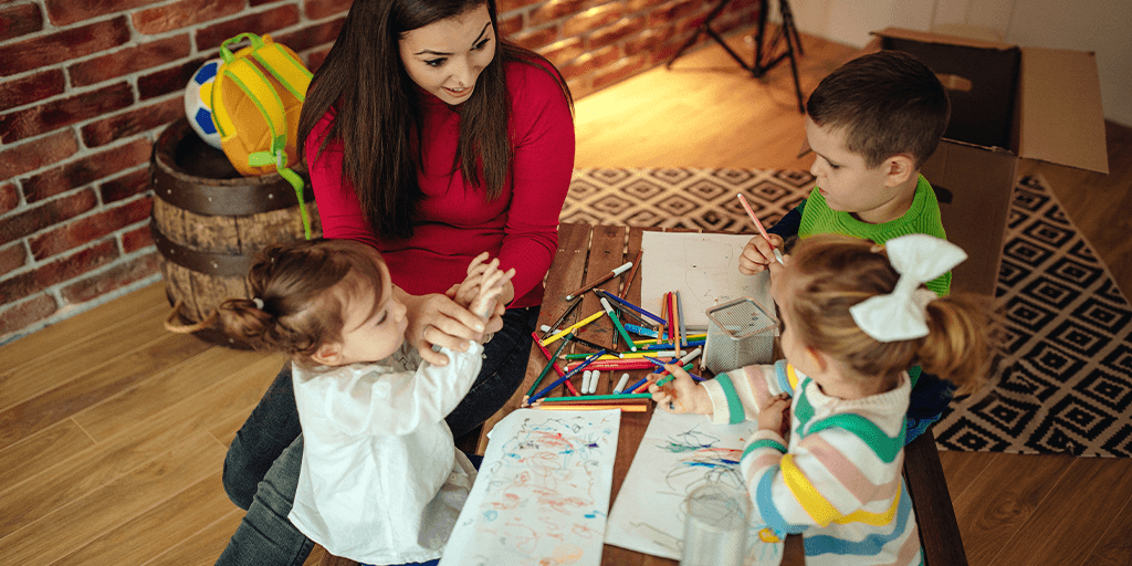 A woman sits at table with children in child care setting