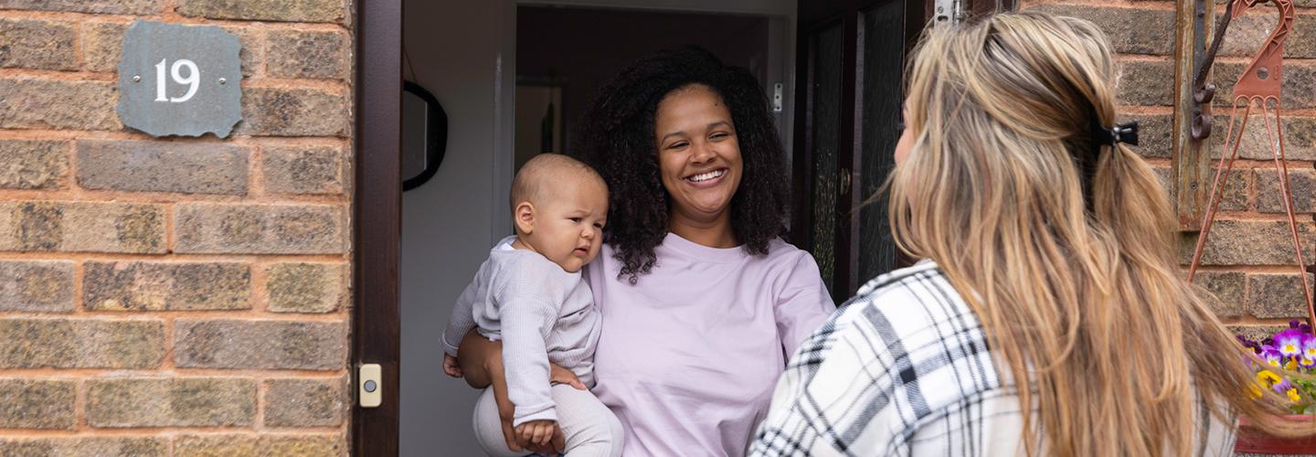 A woman and her child greet a friend at the door