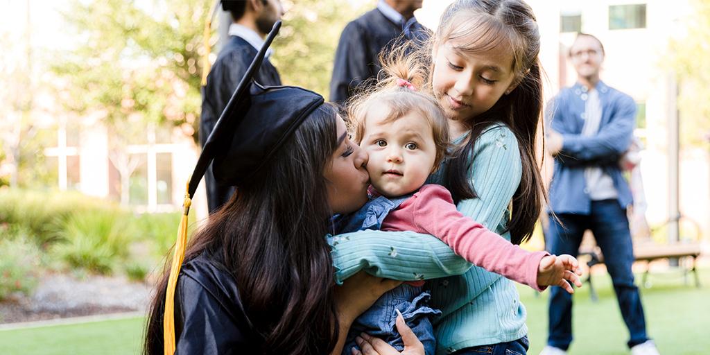 Young adult graduating mother kisses daughter