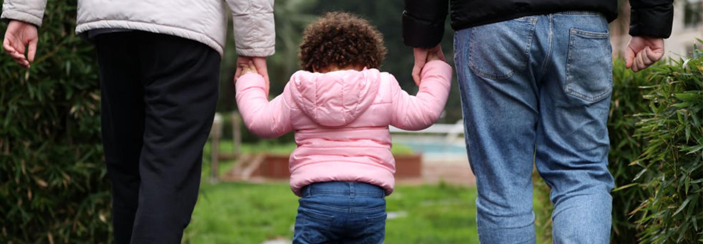 a young girl holds the hands of her parents