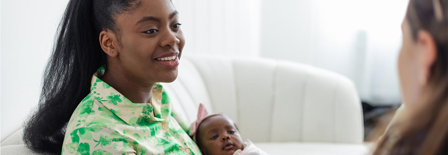 a young woman holds her baby and talks to a nurse